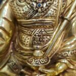 Close up of Guru Rinpoche statue holding a ritual vase in the left hand.