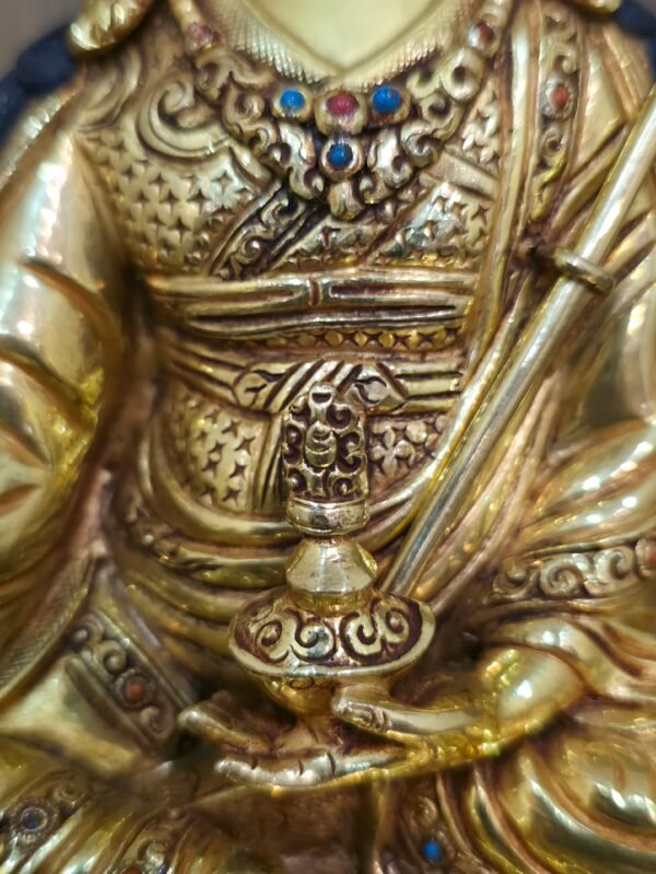 Close up of Guru Rinpoche statue holding a ritual vase in the left hand.
