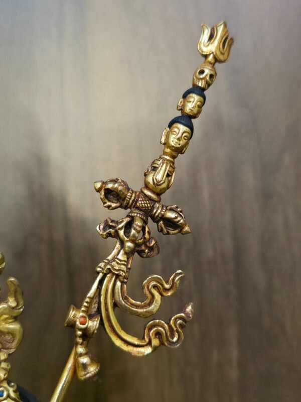 Close up detail of the top of the khatvanga staff featuring heads, skull and a trident.