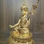 Side angle of Guru Rinpoche statue showing the khatvanga trident staff resting against the left shoulder.