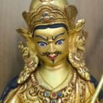 Close up of Guru Rinpoche face hand-painted with gold powder, showing a semi-wrathful expression and mustache.