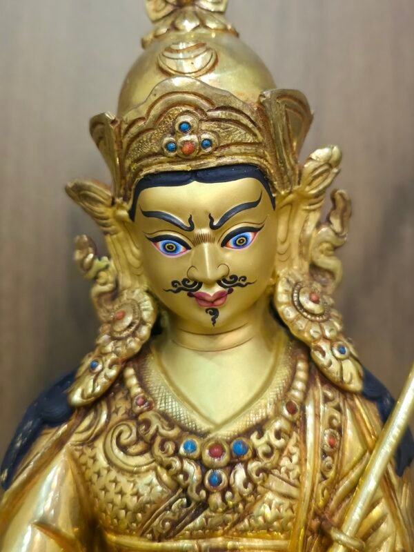 Close up of Guru Rinpoche face hand-painted with gold powder, showing a semi-wrathful expression and mustache.