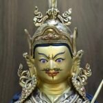 Close up of Guru Rinpoche's hand-painted face featuring a semi-wrathful expression, mustache, and lotus hat.