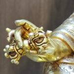 Macro close-up of gold plated Padmasambhava's right hand holding the five-pronged Vajra Dorje symbol.