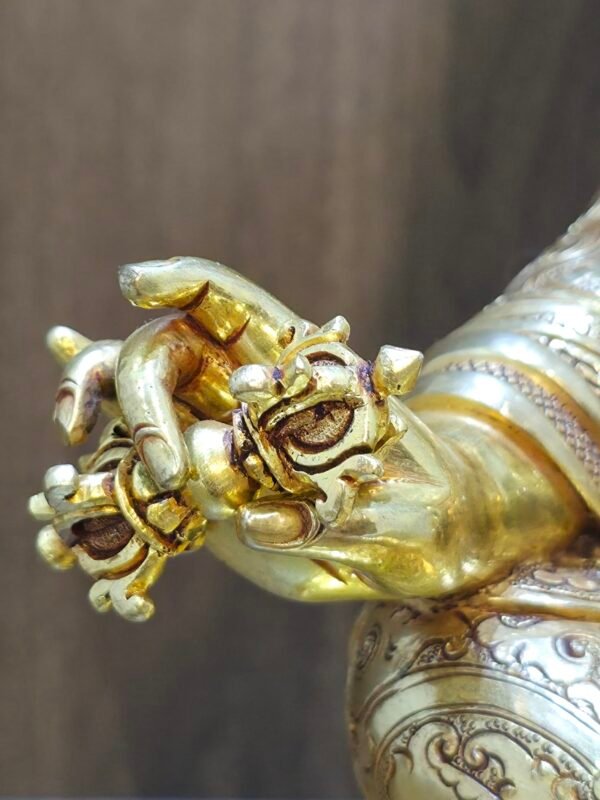 Macro close-up of gold plated Padmasambhava's right hand holding the five-pronged Vajra Dorje symbol.