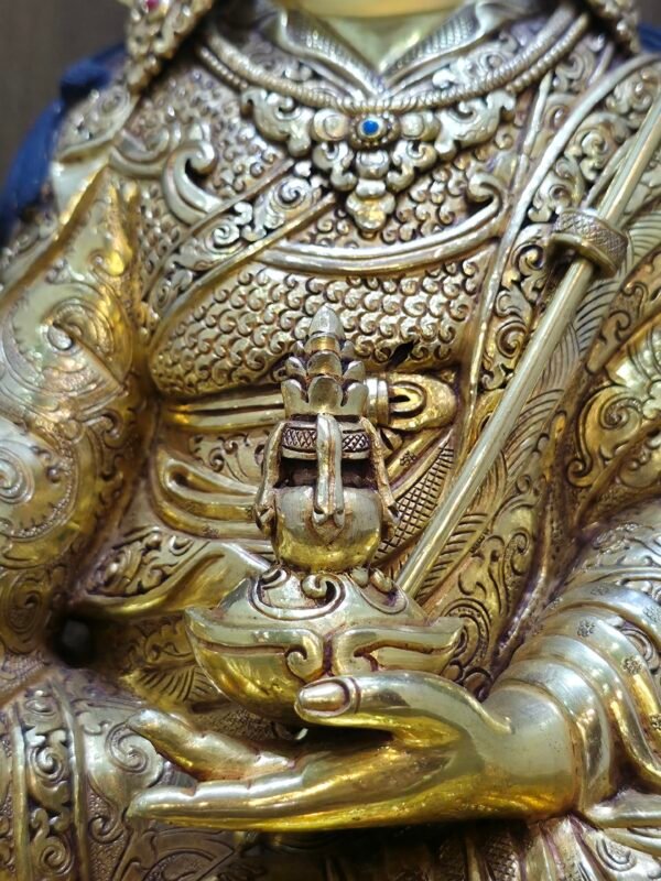 Detail shot of Guru Rinpoche's left hand holding the Kapala skull cup containing the Bumpa long-life vase.