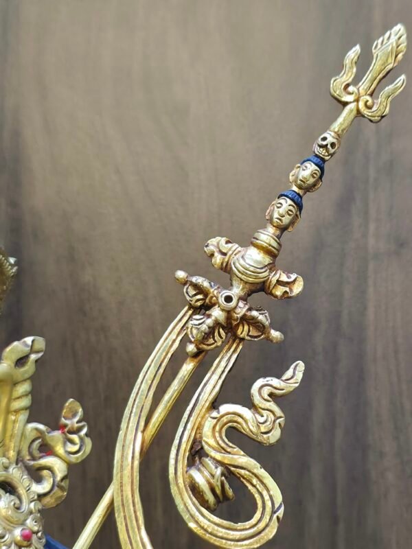 Close up detail of the top of the khatvanga staff featuring a trident and heads and a skull.