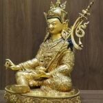 Right side angle of the Lotus Born Guru statue holding a vajra in the right hand and skull cup in the left.