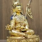 Left side angle of Padmasambhava statue showing the trident staff resting against the shoulder.