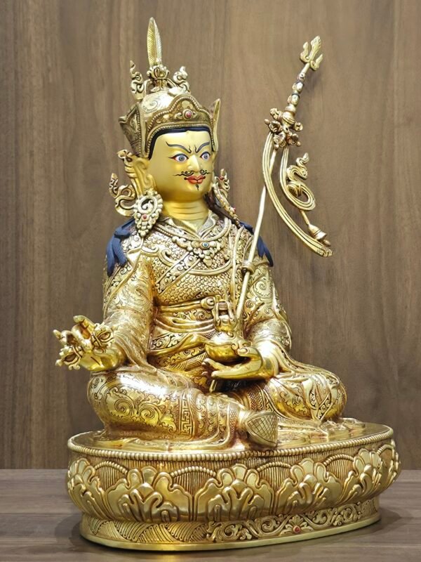 Left side angle of Padmasambhava statue showing the trident staff resting against the shoulder.