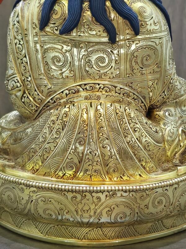 Close up back view of gold plated Guru Rinpoche statue showing intricate floral engravings on the robes and flowing blue hair.