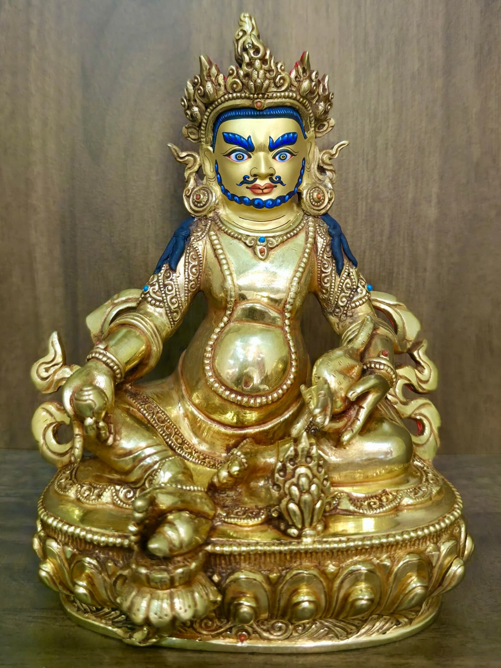 Yellow Dzambhala statue — 24K gold-plated copper; gold-powder face with blue highlights; holds mongoose and citron/wealth fruit on detailed lotus pedestal.