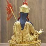 Back view of copper Padmasambhava statue showing flowing blue hair, flaming trident staff, and detailed robe carvings.