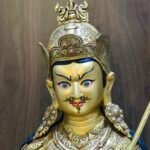 Close up detail of Guru Rinpoche statue face painted with gold dust, showing compassionate expression and intricate crown.