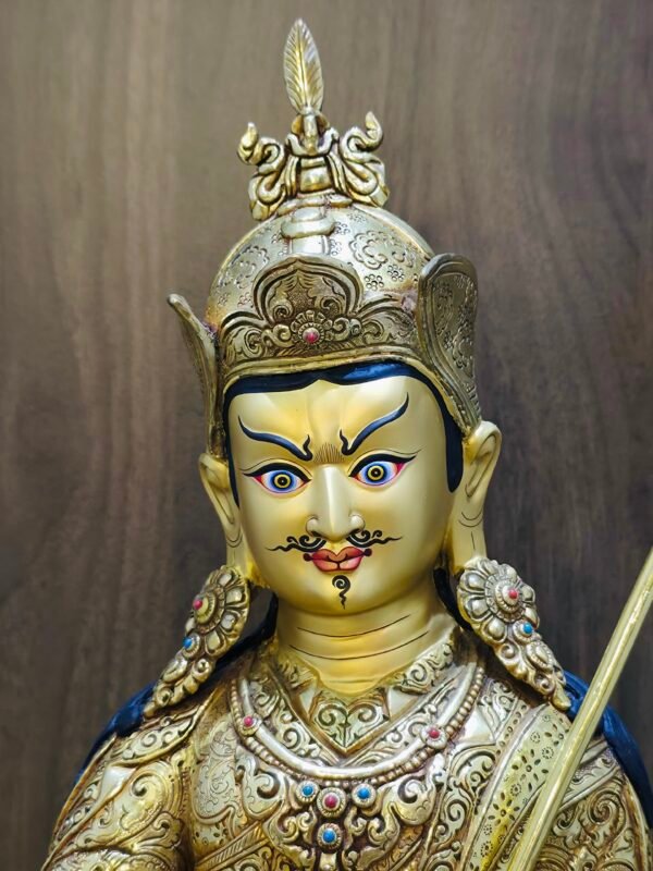 Close up detail of Guru Rinpoche statue face painted with gold dust, showing compassionate expression and intricate crown.