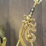 Detail of Khatvanga trident staff on Padmasambhava statue, featuring heads and hanging sash ornaments in gold.