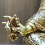 Detail of Padmasambhava statue right hand holding gold Vajra Dorje, showing hand-chased floral patterns on the robes.