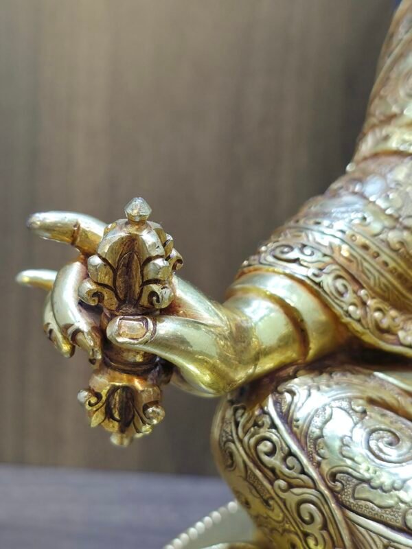 Detail of Padmasambhava statue right hand holding gold Vajra Dorje, showing hand-chased floral patterns on the robes.