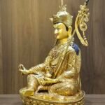 Side profile view of gold plated Guru Rinpoche statue showing the Khatvanga staff and ear ornaments.