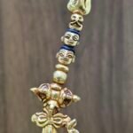 Close up detail of the top of the khatvanga staff featuring a trident and heads and a skull.