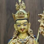 Close up of Guru Rinpoche statue face with gold powder painting, showing semi-wrathful expression and lotus hat.