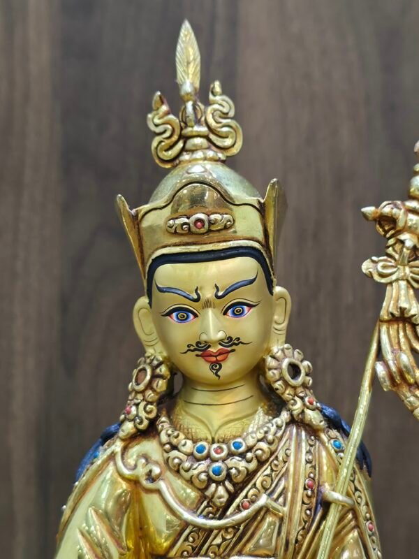 Close up of Guru Rinpoche statue face with gold powder painting, showing semi-wrathful expression and lotus hat.