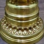 Close-up of gold-plated copper Tibetan chorten stupa base with lotus petals and engraved band.