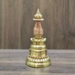 Full-length gold-plated copper Tibetan chorten stupa centered on table with wood backdrop.