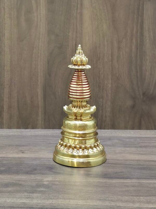 Full-length gold-plated copper Tibetan chorten stupa centered on table with wood backdrop.
