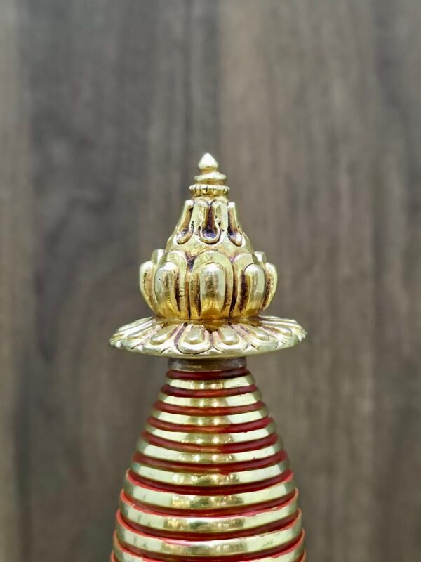 Finial detail of gold-plated copper Tibetan stupa with lotus top and red-banded spire.