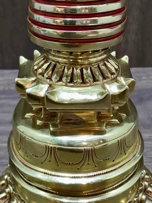 Midsection detail of gold-plated copper chorten with stepped base and red-banded body.