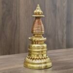 Full view gold-plated copper Tibetan chorten stupa with red bands on table, angled shot.