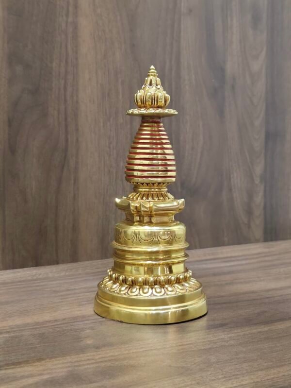 Full view gold-plated copper Tibetan chorten stupa with red bands on table, angled shot.