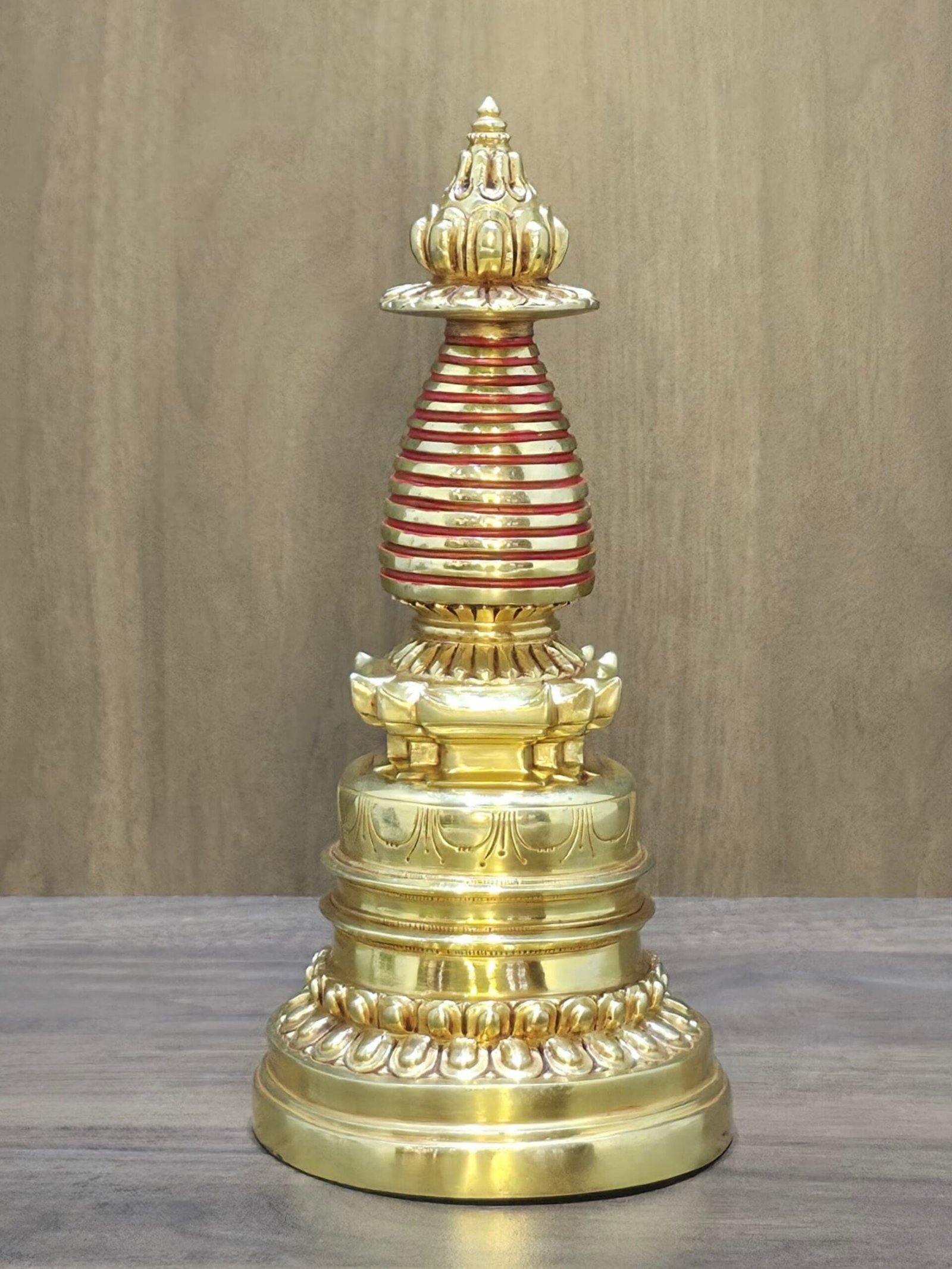 Centered full-length gold-plated copper Tibetan stupa (chorten) with red bands on table.