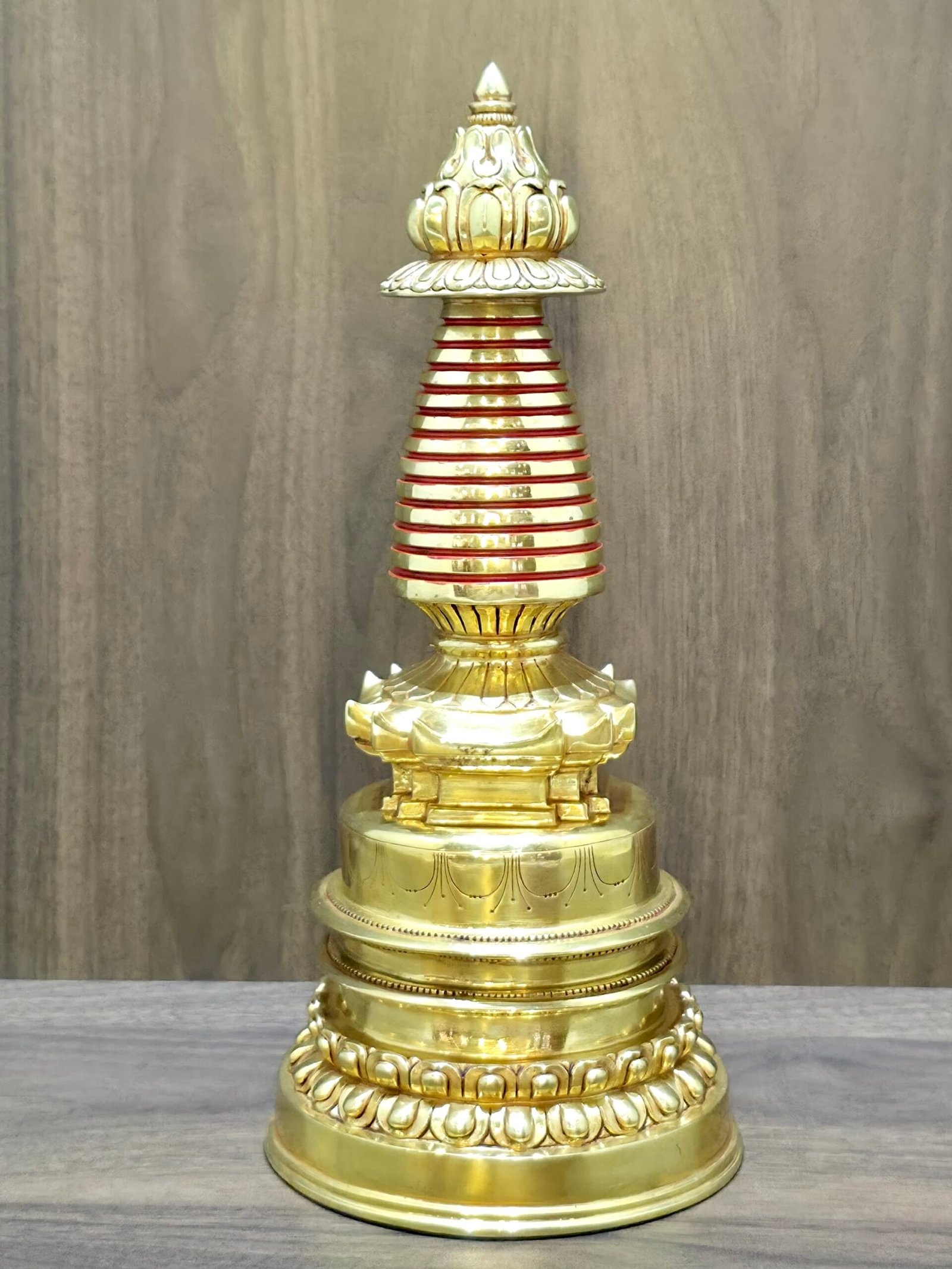 S004-4:3-1 Gold plated copper Tibetan stupa with red spire bands, front view on tabletop against wood panel.