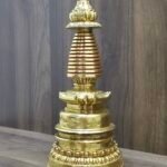 Angled view of gold plated copper Tibetan stupa on tabletop, showing side profile of lotus base and spire.
