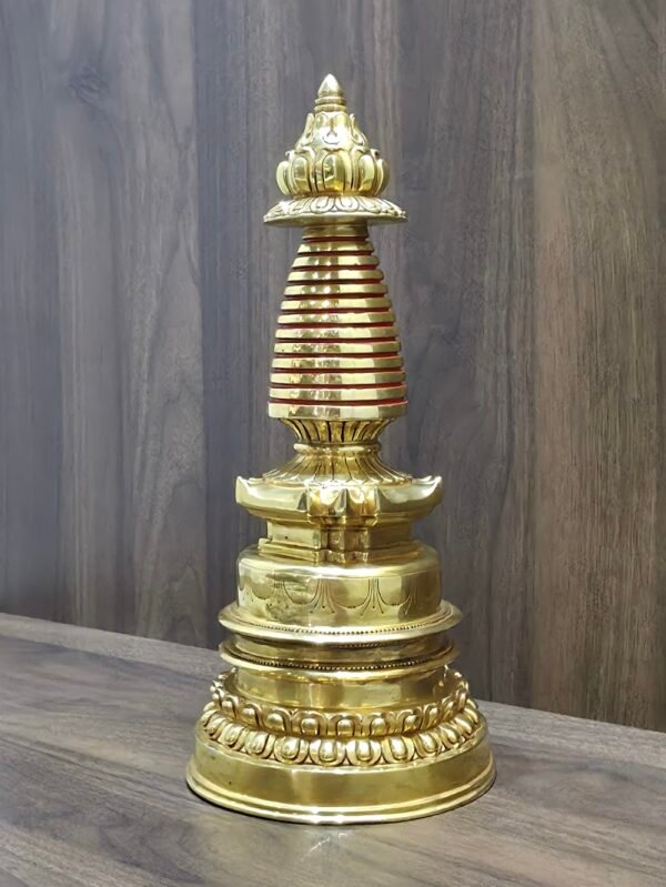 Angled view of gold plated copper Tibetan stupa on tabletop, showing side profile of lotus base and spire.