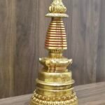 Right angled view of gold plated copper Tibetan stupa on tabletop, showing red spire rings and tiered base.