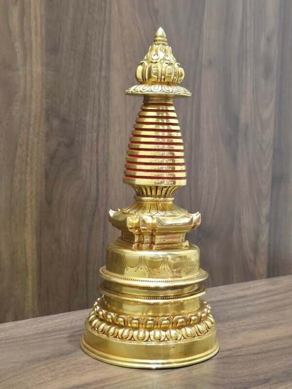 Right angled view of gold plated copper Tibetan stupa on tabletop, showing red spire rings and tiered base.