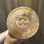 Underside of stupa base showing copper bottom plate with raised vajra emblem, held in hands.