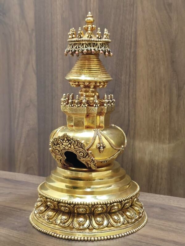 Angled left view of gold plated copper stupa showing torana arch window, rounded body, and ringed spire under jeweled canopy.
