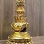 Angled right view of gold plated copper stupa showing carved arch window, stepped base, and detailed canopy with inlays.