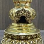Close up of carved torana arch opening and stepped base of gold plated copper stupa, with lotus petal detailing.