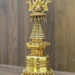 Right angled view of gold plated copper Tibetan stupa, showing stepped base and ringed spire profile.