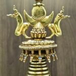 Close up of stupa top, jewelled crown with crescent and flame finial, small dangling ornaments under the rim.
