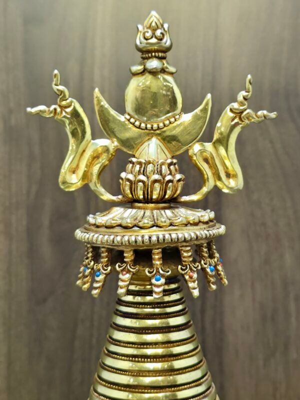 Close up of stupa top, jewelled crown with crescent and flame finial, small dangling ornaments under the rim.