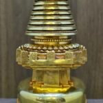 Detail of the upper midsection, striped conical spire and square platform with carved edging, gold plated finish.