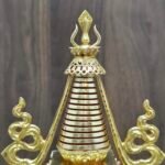 Close view of the upper spire showing red ring bands, pierced parasol style canopy, and finial detail in gold plating.