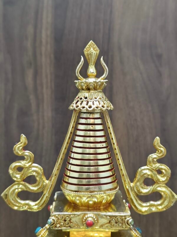 Close view of the upper spire showing red ring bands, pierced parasol style canopy, and finial detail in gold plating.