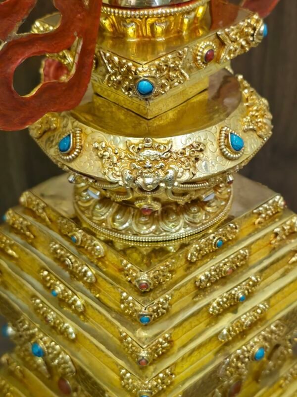 Close up of the stupa’s stepped base showing engraved panels, raised floral trim, and small blue and red inlay accents.